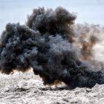 Dark smoke cloud rising from sandy beach.