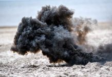 Dark smoke cloud rising from sandy beach.