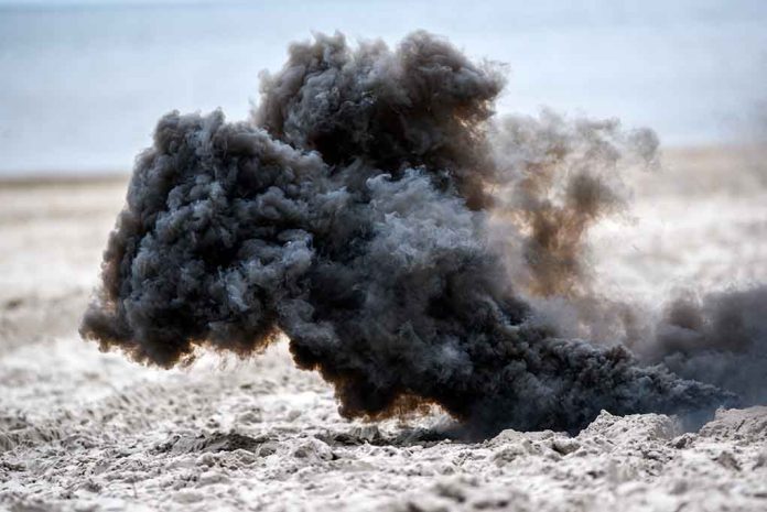 Dark smoke cloud rising from sandy beach.