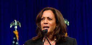 Woman speaking behind a podium with blue backdrop.