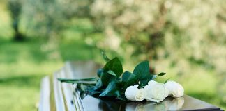 White roses on a polished wooden casket outdoors.