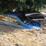 Two cars submerged in muddy floodwaters.