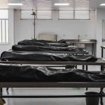 Covered bodies on metal tables in a morgue.