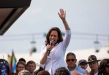 Woman speaking at outdoor event with raised hand.