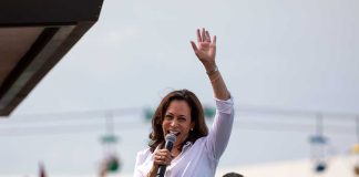 Woman speaking at outdoor event with raised hand.