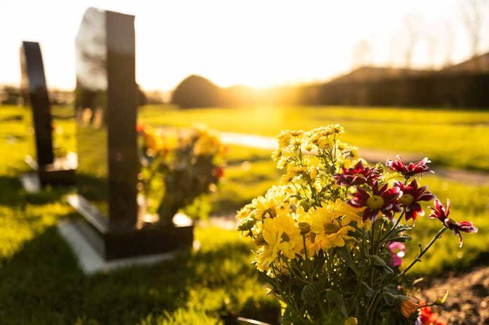 Sunlit cemetery with flowers on headstone.