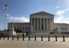 Supreme Court building with flag and people outside.