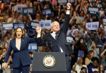 Two people celebrate on stage with supporters behind.