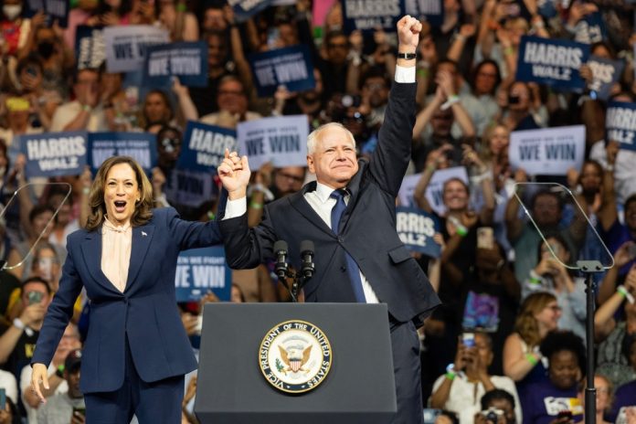 Two people celebrate on stage with supporters behind.