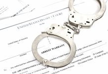 Handcuffs on top of an arrest warrant document.