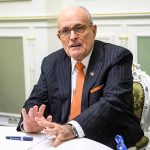 Man in suit talking at a table indoors.