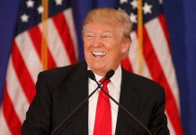 Man smiling at podium with American flags in background.