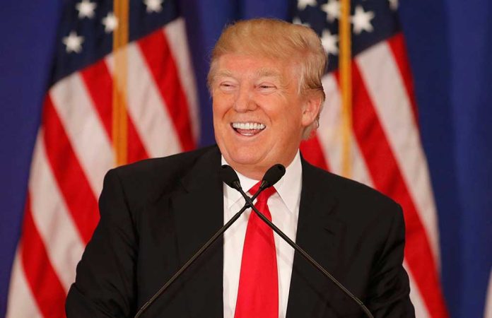 Man smiling at podium with American flags in background.