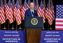 President Joe Biden speaks behind podium with American flags.