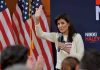 Woman speaking into microphone beside American flags.