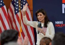 Woman speaking into microphone beside American flags.