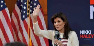 Woman speaking into microphone beside American flags.