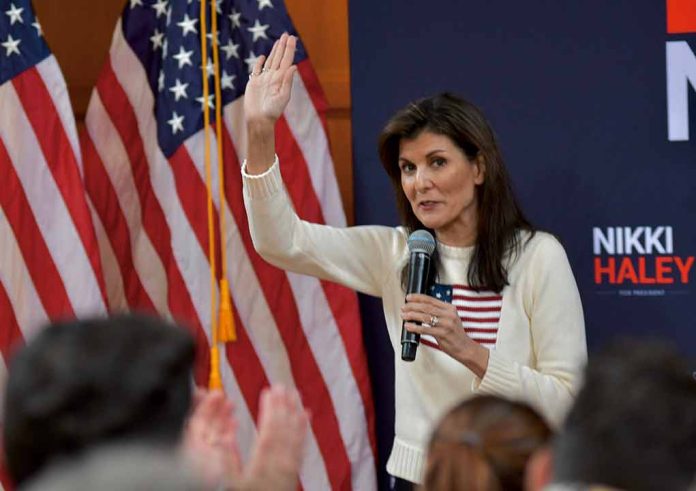 Woman speaking into microphone beside American flags.