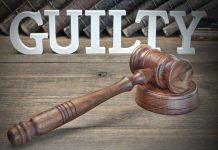 Judge's gavel and "GUILTY" sign on wooden table.