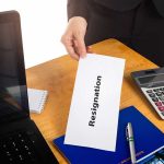 Hand holding a resignation letter on desk.