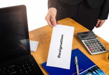 Hand holding a resignation letter on desk.