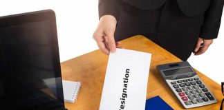 Hand holding a resignation letter on desk.