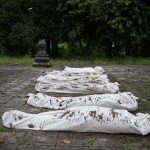 Five wrapped bodies on ground surrounded by trees.