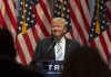 Person speaking at podium with American flags behind.