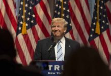 Person speaking at podium with American flags behind.