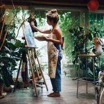 Artist painting on canvas in plantfilled studio