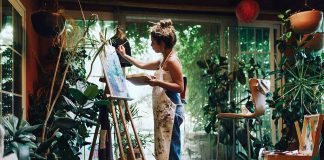 Artist painting on canvas in plantfilled studio