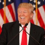 Man smiling at podium with American flags in background.