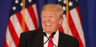 Man smiling at podium with American flags in background.