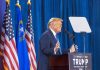 Person speaking at podium with flags in background.