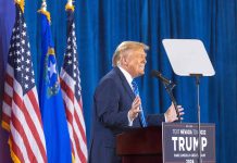 Person speaking at podium with flags in background.