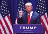 Man speaking at podium with American flags behind.