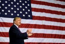 Man clapping in front of large American flag