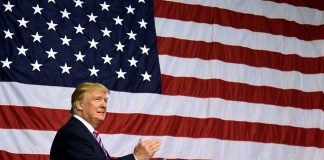 Man clapping in front of large American flag