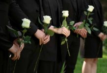 People in black holding white roses in a line.