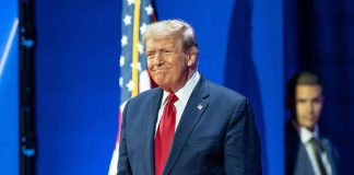 Man in suit next to American flag.