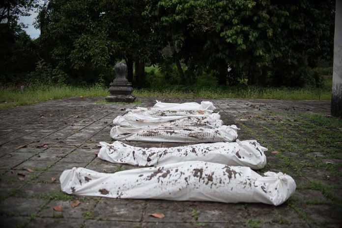 Five wrapped bodies on ground surrounded by trees.