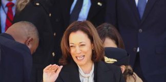 Smiling woman in black coat waves among people.