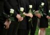 People in black holding white roses in a line.