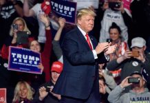 Man clapping on stage surrounded by supporters holding signs