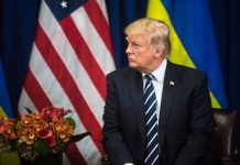 Man in suit sitting near US and Ukrainian flags