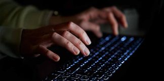 Hands typing on a backlit keyboard in darkness