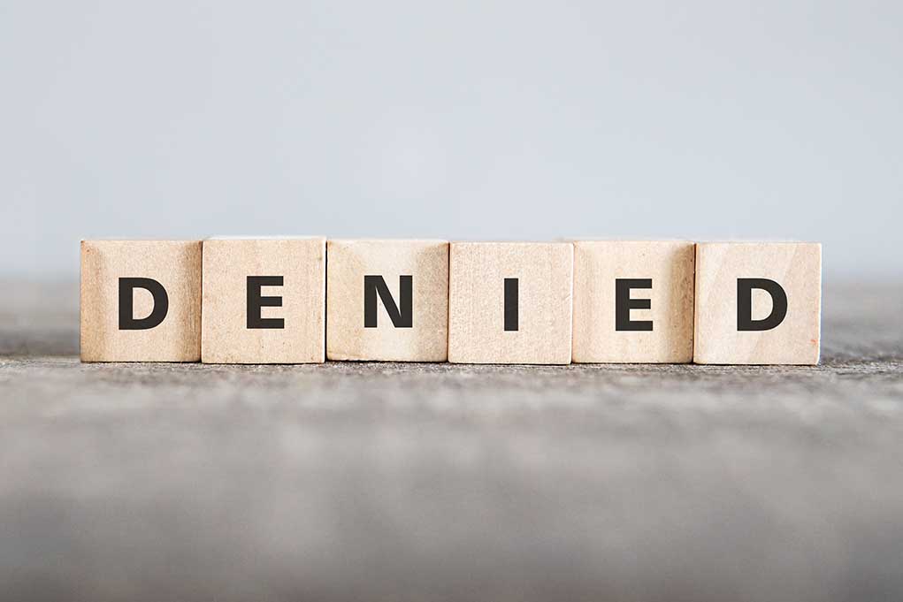 Wooden blocks spelling out DENIED in bold letters.