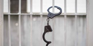 Open handcuff hanging on white prison bars
