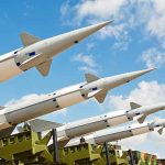 Multiple missiles pointed upward on launchers against blue sky