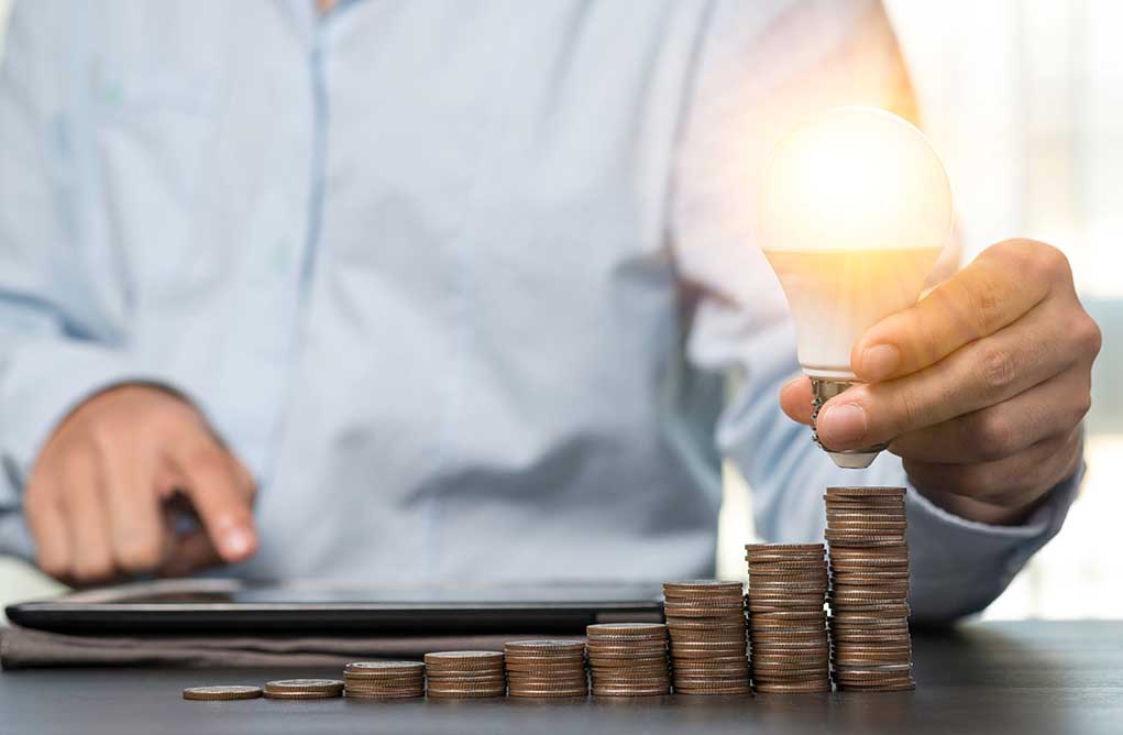 Light bulb held above stacked coins on table